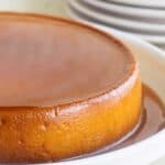 a side view of a puerto rican flan de queso with a lot of caramel and a few plates with forks on the background.
