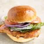 a grilled chicken sandwich made on a potato bread, mayo, lettuce, tomato and onions.