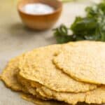 a stack of plantain tortillas with a dish with salt and parsley on the background.
