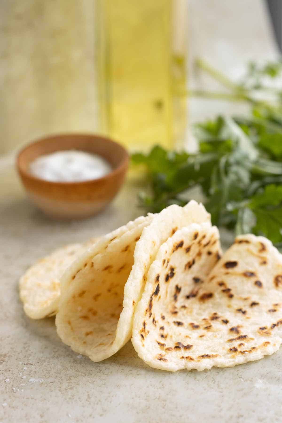 3 tortillas de yuca dobladas en forma de taco con un envase con sal, una botella de aceite y perejil en el fondo.