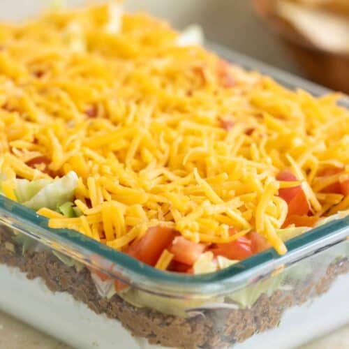 a mold full of a puerto rican 5 layer dip with a bowl of chips in the background and a few on the side.