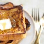 a plate with a stack of 3 coconut french toast with a couple of forks on the side.