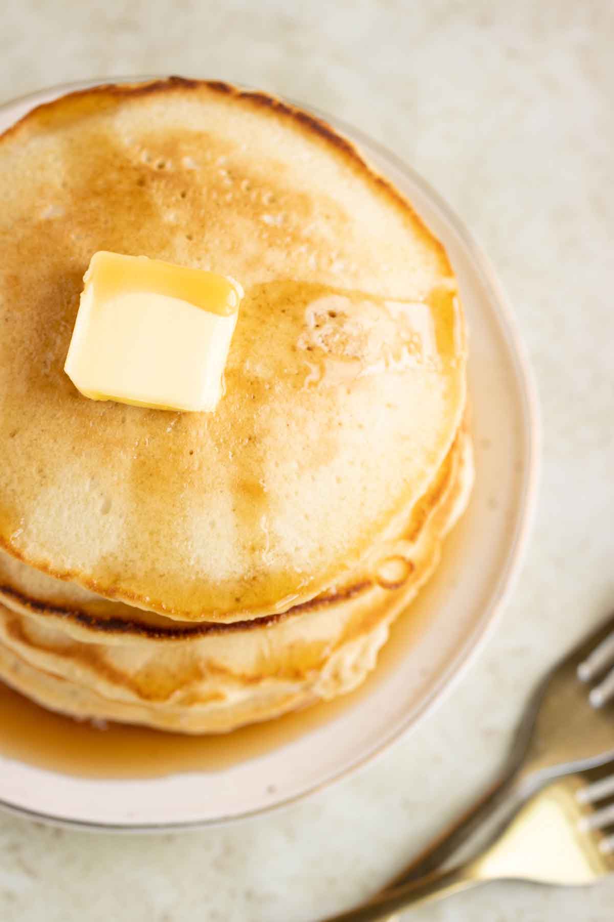 A view of a stack of coconut milk pancakes from the top on a plate with syrup and butter with a couple of forks in the side.
