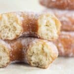 a sugar donut cut in half and a stack of fried donuts on the background.