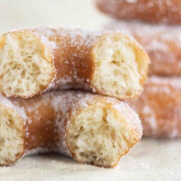 a sugar donut cut in half and a stack of fried donuts on the background.