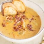 a big bowl of potato and carrot soup with some bread a bacon as toppings.