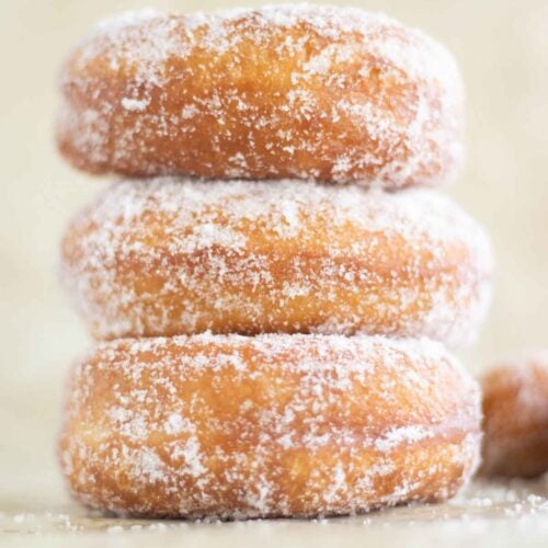 a stack of 3 fried sugar donuts and a couple of donut holes on the side.