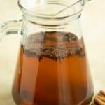 a glass pitcher full of the coquito tea with spices in it.