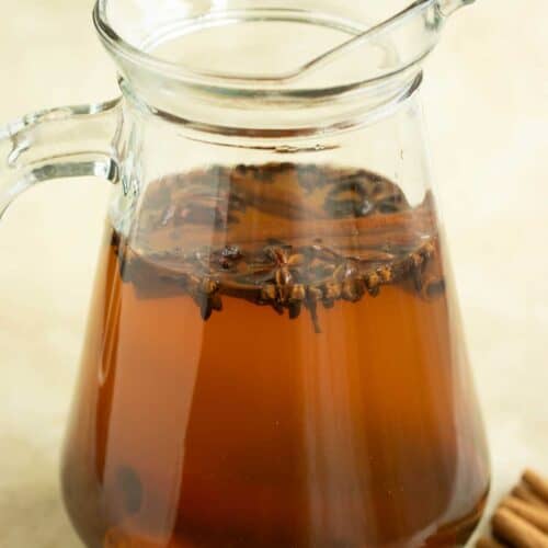 a glass pitcher full of the coquito tea with spices in it.