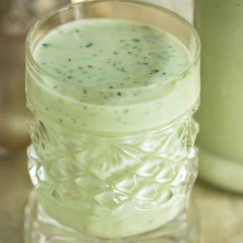 a cup with mint coquito and a bottle on the background.