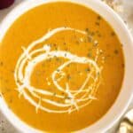 a bowl of creamy coconut pumpkin soup with cream and croutons on top and a couple of spoons on the side.