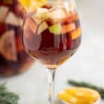 A wine glass of a Spanish Sangria with a piece of orange as decoration and a big jar on the back.