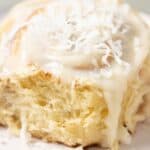 A coconut cinnamon rolls with a coconut cream cheese frosting and coconut flakes on top.