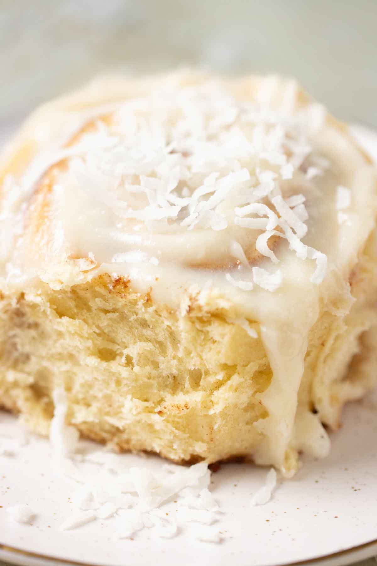 A coconut cinnamon rolls with a coconut cream cheese frosting and coconut flakes on top.