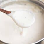 Cream cheese white sauce in a steel pan with a spoonful of the cream cheese bechamel.