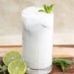 A tall glass with a mojito de coco also known as coconut mojito with mint leaves as garnish a half lime next to the glass.