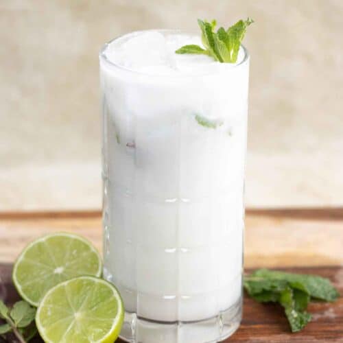 A tall glass with a mojito de coco also known as coconut mojito with mint leaves as garnish a half lime next to the glass.