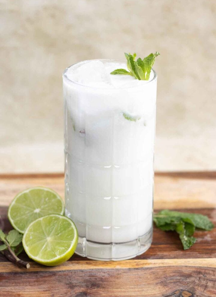 A tall glass with a mojito de coco also known as coconut mojito with mint leaves as garnish a half lime next to the glass.