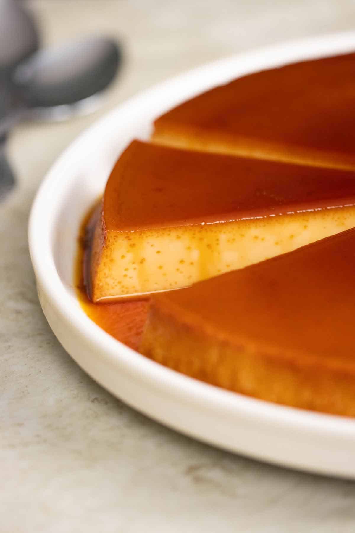 a big plate with a few big pieces of quesillo with a couple of spoons on the side.