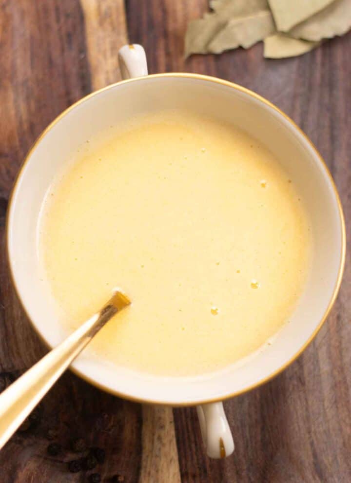 a small dish with a spiced beurre blanc with a few bay leaves on the side and a spoon inside the dish.