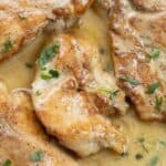 chicken breast in a white sauce spiced beurre blanc garnished with parsley.