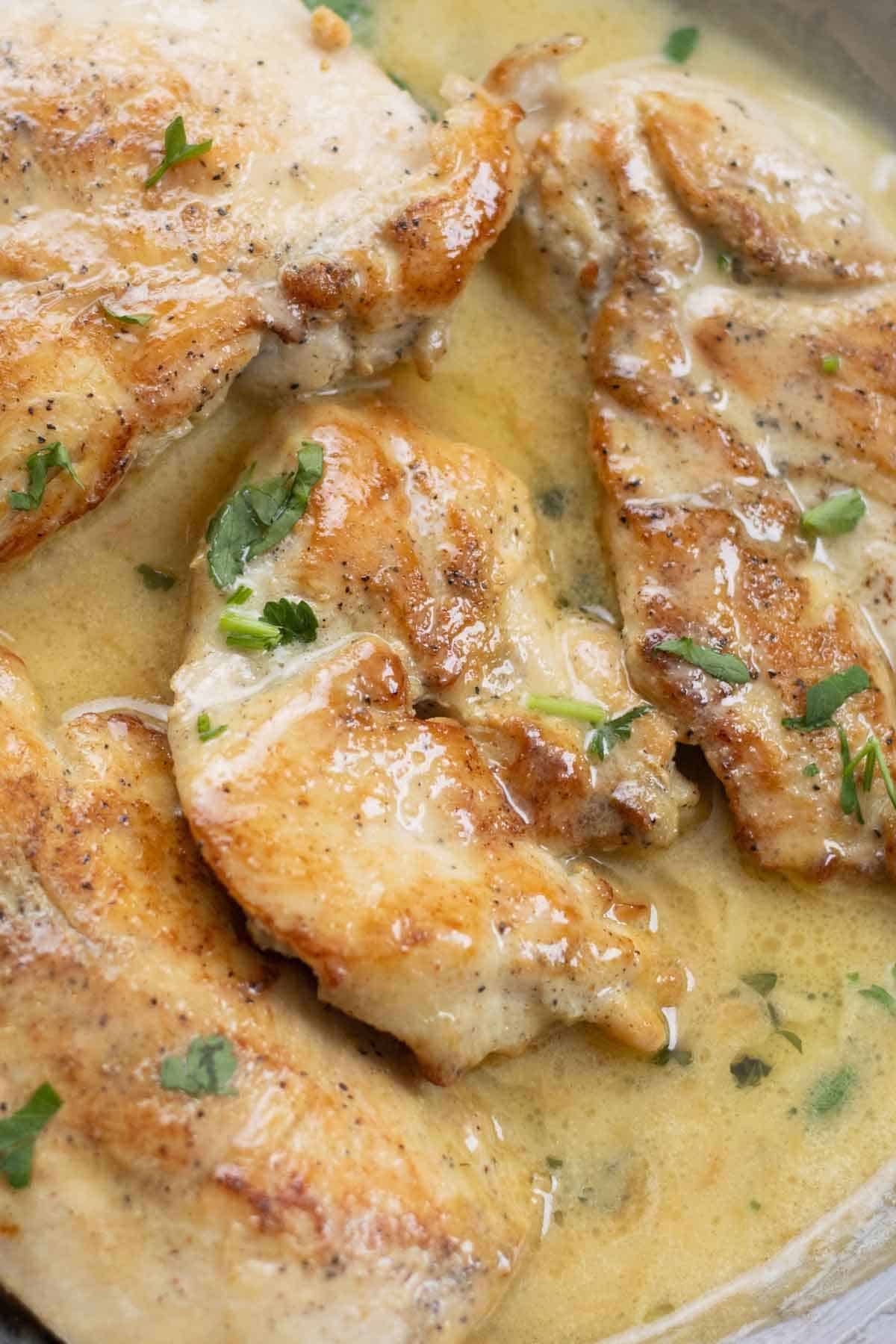 chicken breast in a white sauce spiced beurre blanc garnished with parsley.