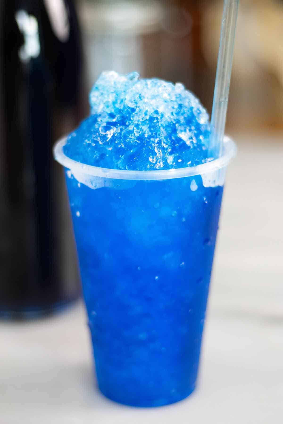 A cup with a Puerto Rican piragua de pitufo or a blueberry piragua made with the blueberry syrup on the background.
