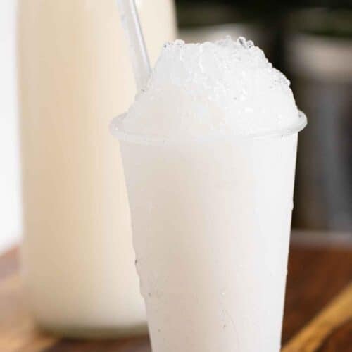 A Puerto Rican piragua de coco or a coconut shaved ice and a bottle of coconut syrup on the background.