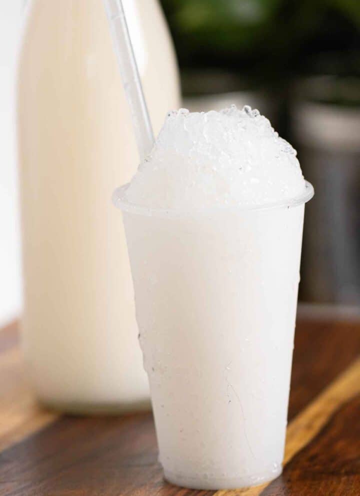A Puerto Rican piragua de coco or a coconut shaved ice and a bottle of coconut syrup on the background.