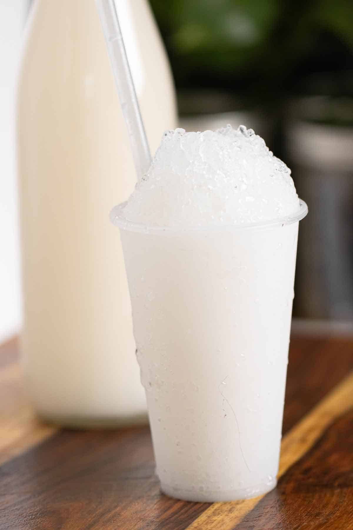 A Puerto Rican piragua de coco or a coconut shaved ice and a bottle of coconut syrup on the background.