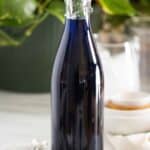 A bottle of a homemade blueberry syrup with a few measuring spoons on the side.