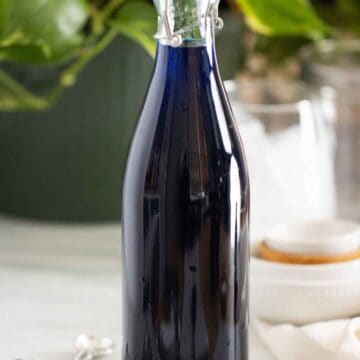 A bottle of a homemade blueberry syrup with a few measuring spoons on the side.