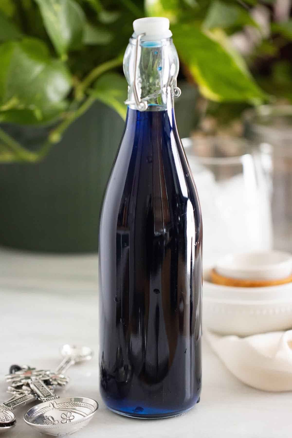 A bottle of a homemade blueberry syrup with a few measuring spoons on the side.
