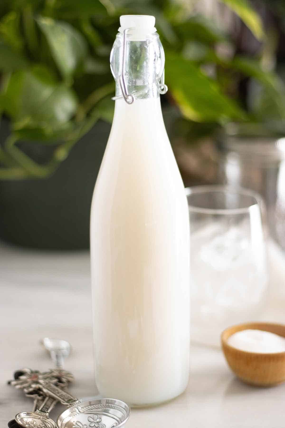 A bottle of a homemade coconut syrup with a few measuring spoons on the side.