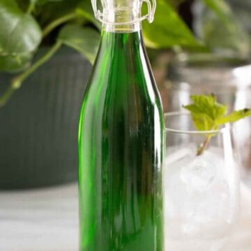 A bottle with a homemade mint syrup with a cup with fresh mint on the back.