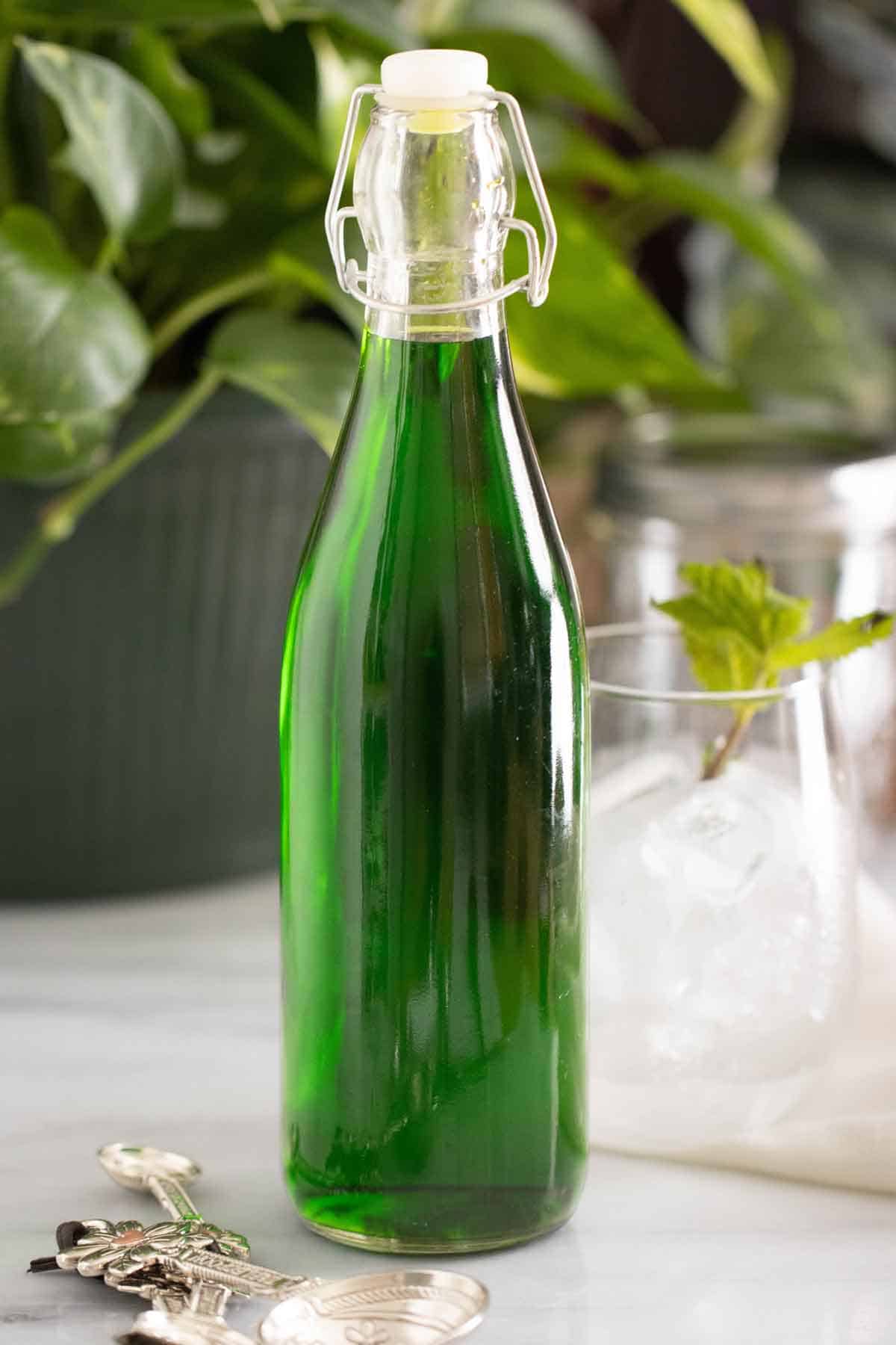 A bottle with a homemade mint syrup with a cup with fresh mint on the back.