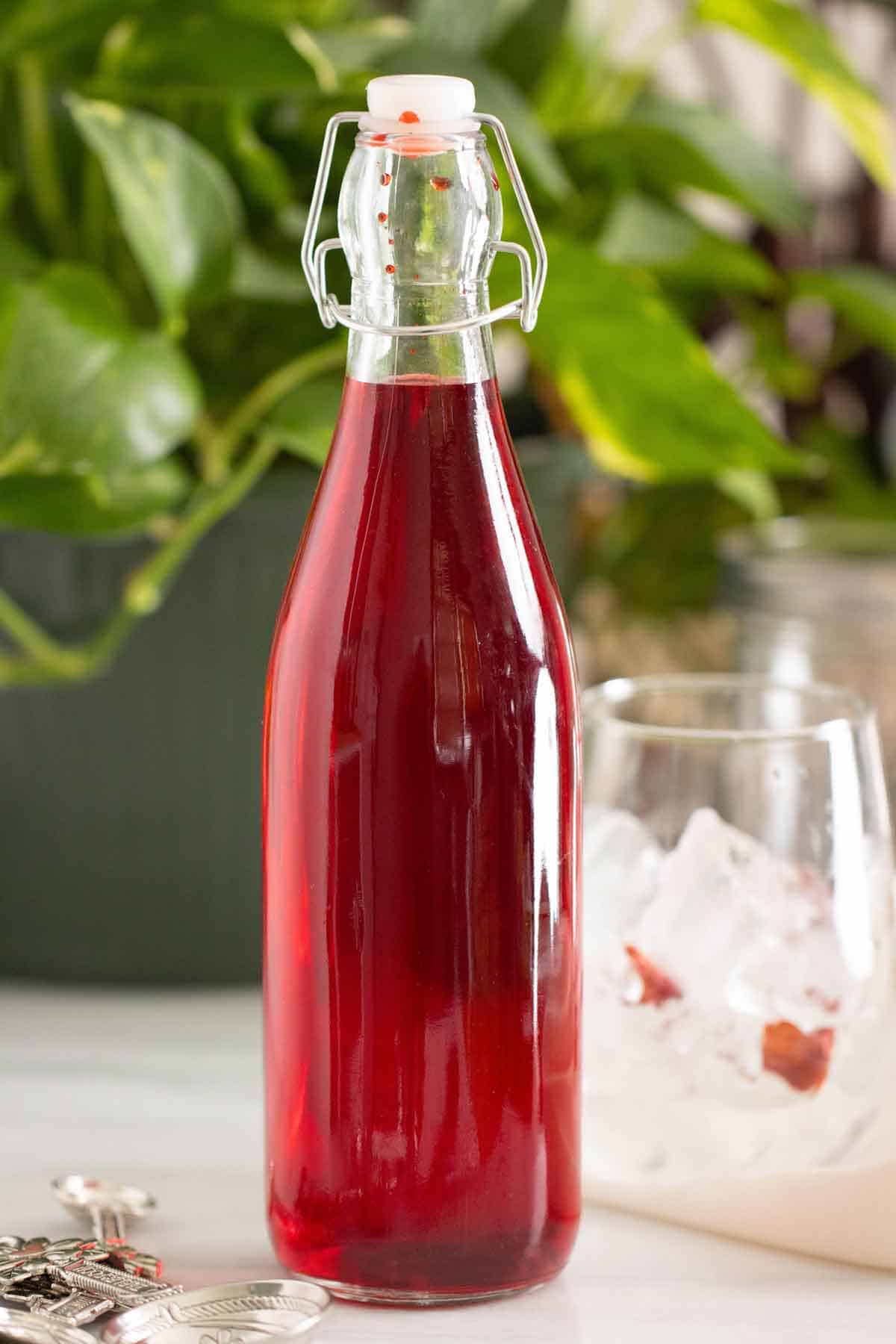 A bottle of a homemade strawberry syrup with a cup on the side.
