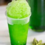 A mint flavor piragua with a fresh mint on the side and a syrup bottle on the background.