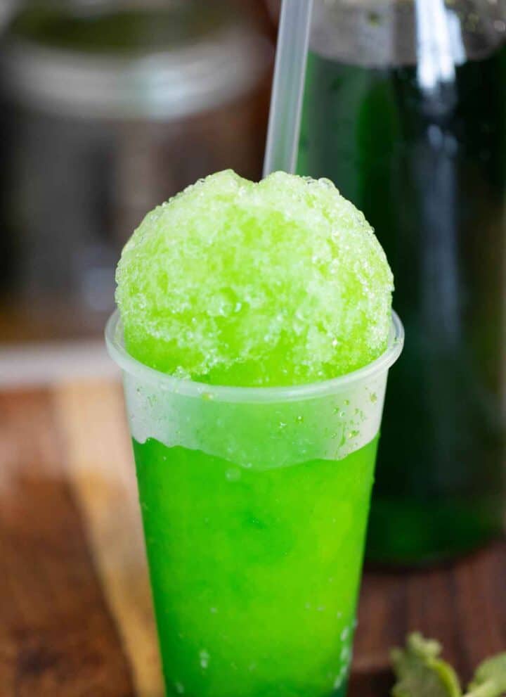 A mint flavor puerto rican piragua or mint shaved ice with a syrup bottle on the back.