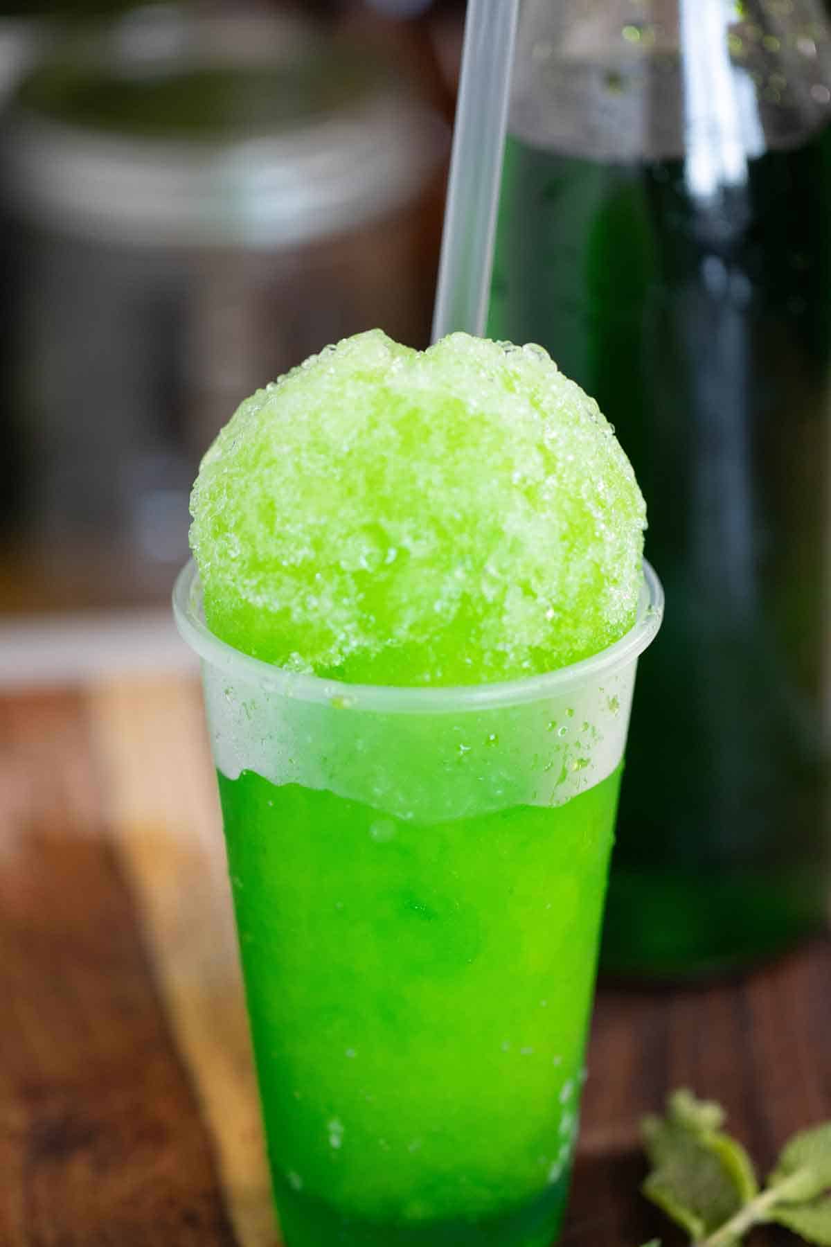 A mint flavor puerto rican piragua or mint shaved ice with a syrup bottle on the back.