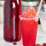 A Puerto Rican strawberry piragua or shaved ice with a few pieces of strawberries on the side and syrup on the side.