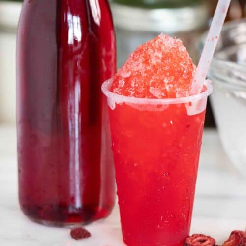 A Puerto Rican strawberry piragua with a few pieces of strawberries on the side and syrup on the side.