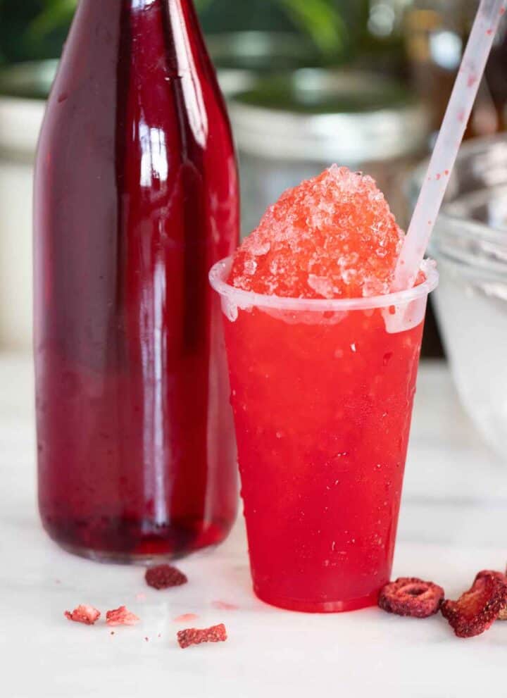 A Puerto Rican strawberry piragua or shaved ice with a few pieces of strawberries on the side and syrup on the side.