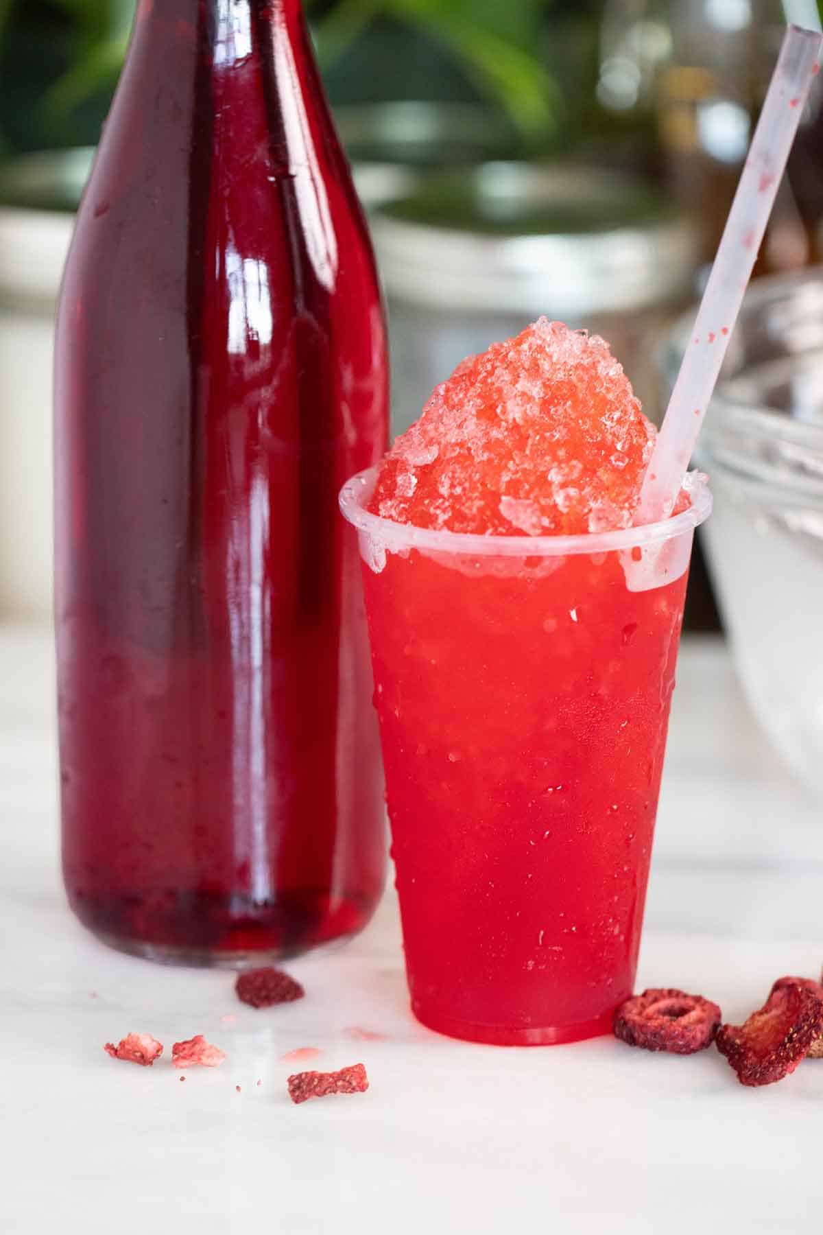 A Puerto Rican strawberry piragua or shaved ice with a few pieces of strawberries on the side and syrup on the side.
