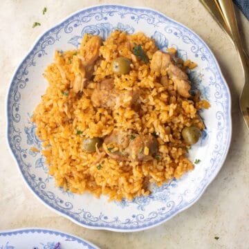 A plate with the arroz con pollo with a a plate with a side of red cabbage and a couple of forks.