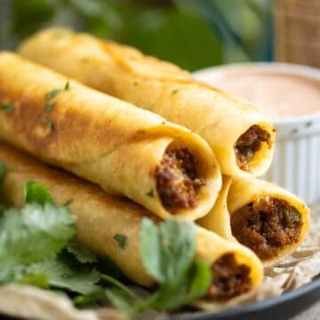 a pan with beef taquitos with a sauce on the side and fresh cilantro.