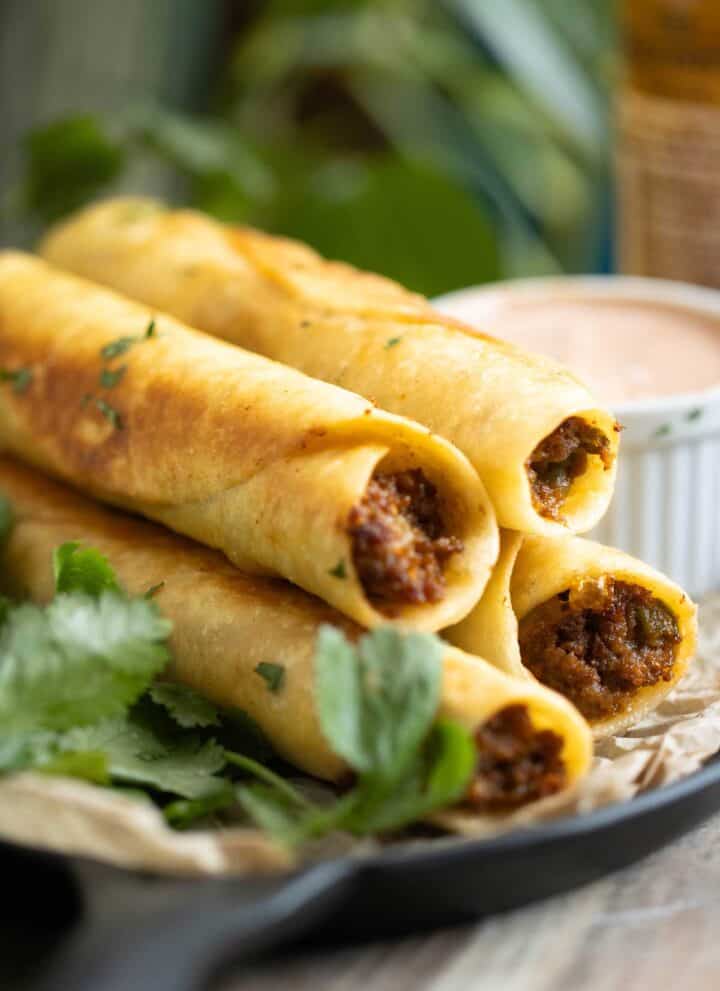 a pan with beef taquitos with a sauce on the side and fresh cilantro.
