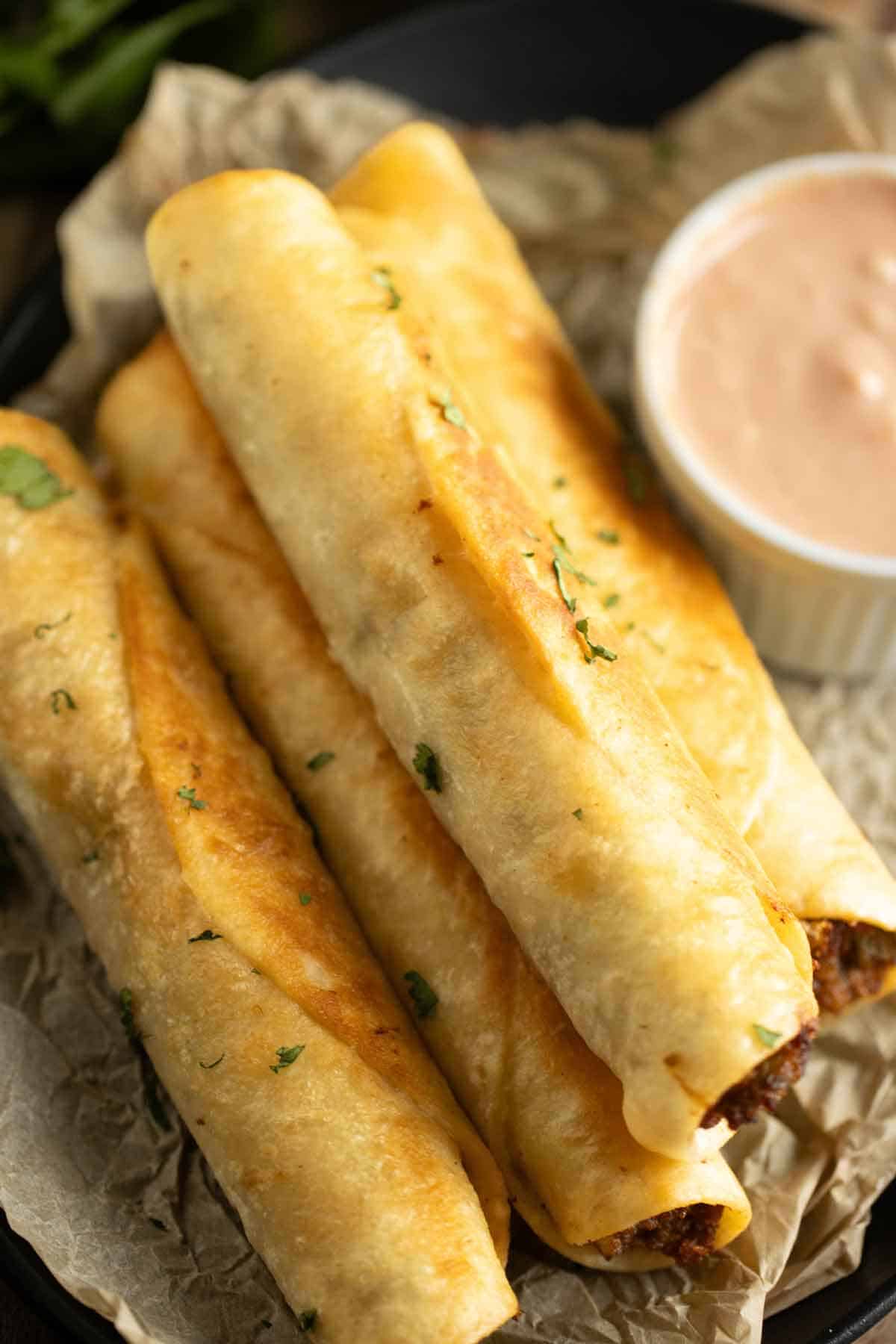 A pan with a few beef flautas and a chipotle sauce on the side.