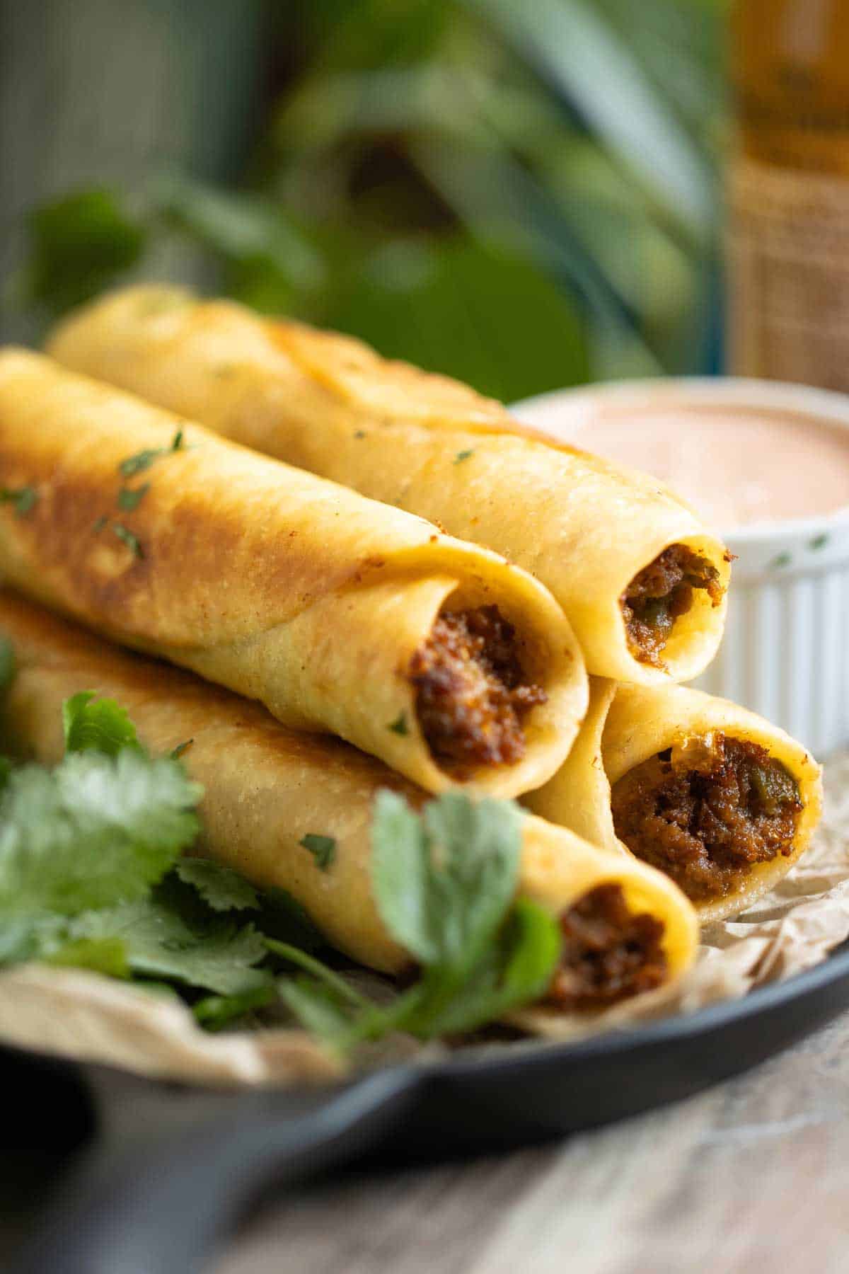 a pan with beef taquitos with a sauce on the side and fresh cilantro.