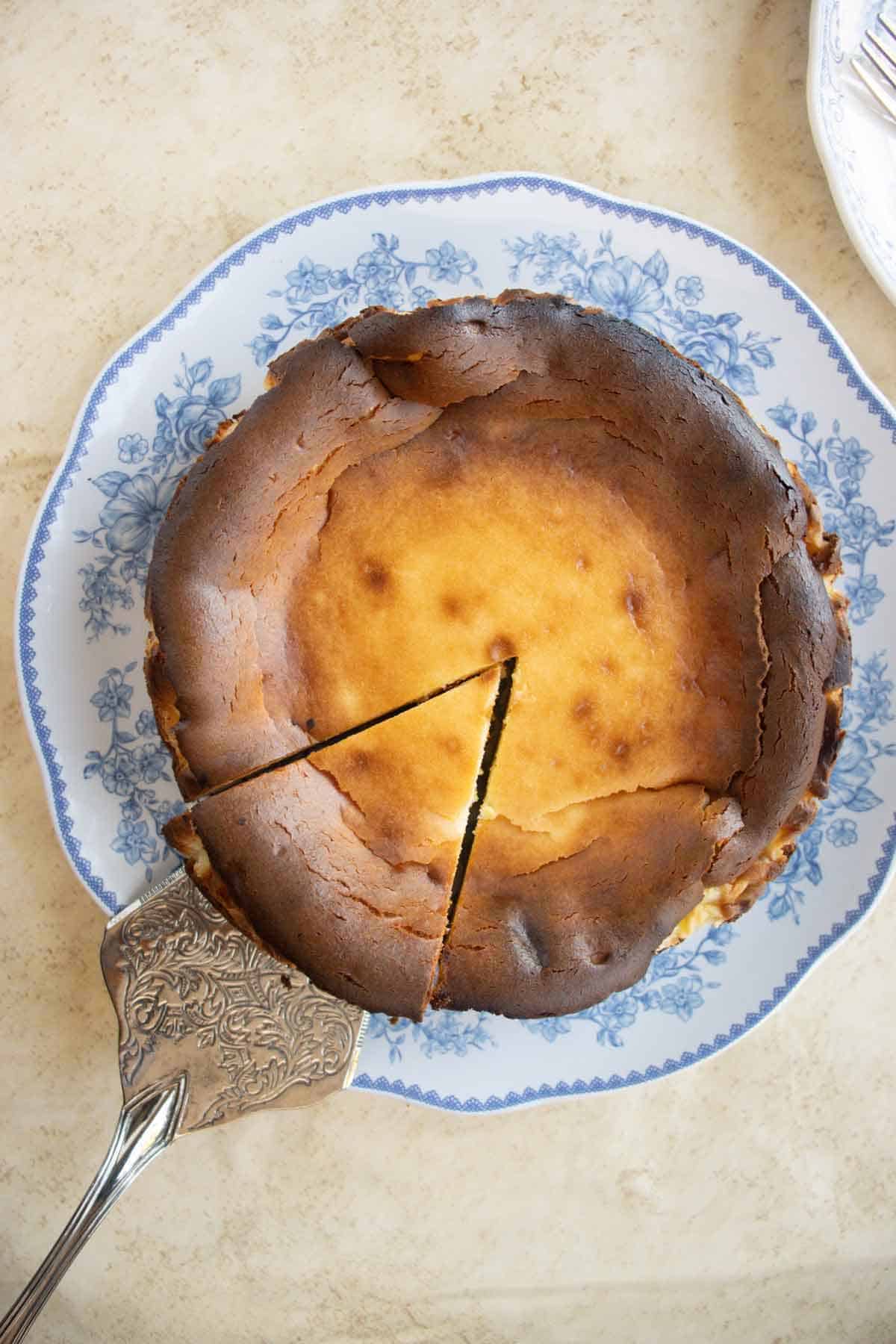 A plate with a basque cheesecake with a piece of cheesecake cut on a cake spatula.